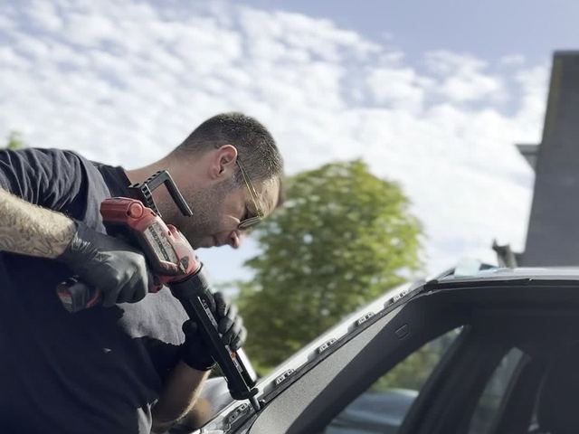 Tekniker arbejder ved forrudens karm, set nedefra mod himlen